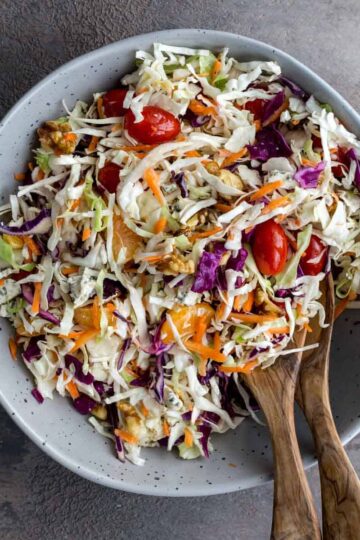 Overhead of mayo free coleslaw in a large grey bowl with wooden salad servers.