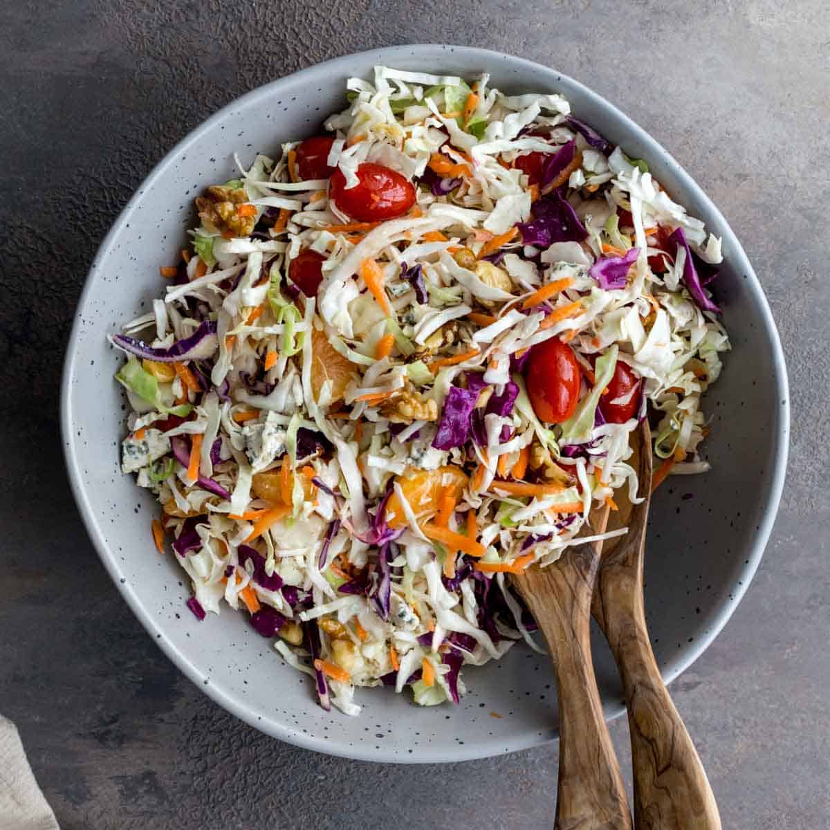 Overhead of mayo free coleslaw in a large grey bowl with wooden salad servers.