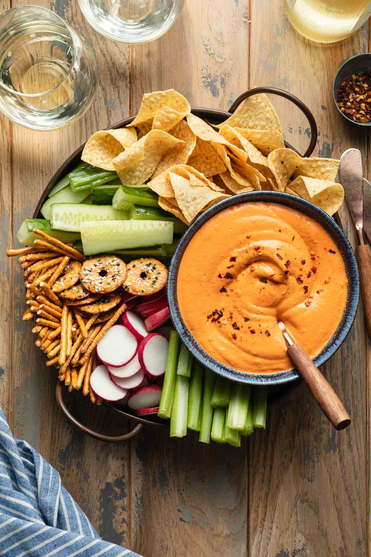Overhead view of roasted pepper dip served with a tray of veggies, chips and pretzels.