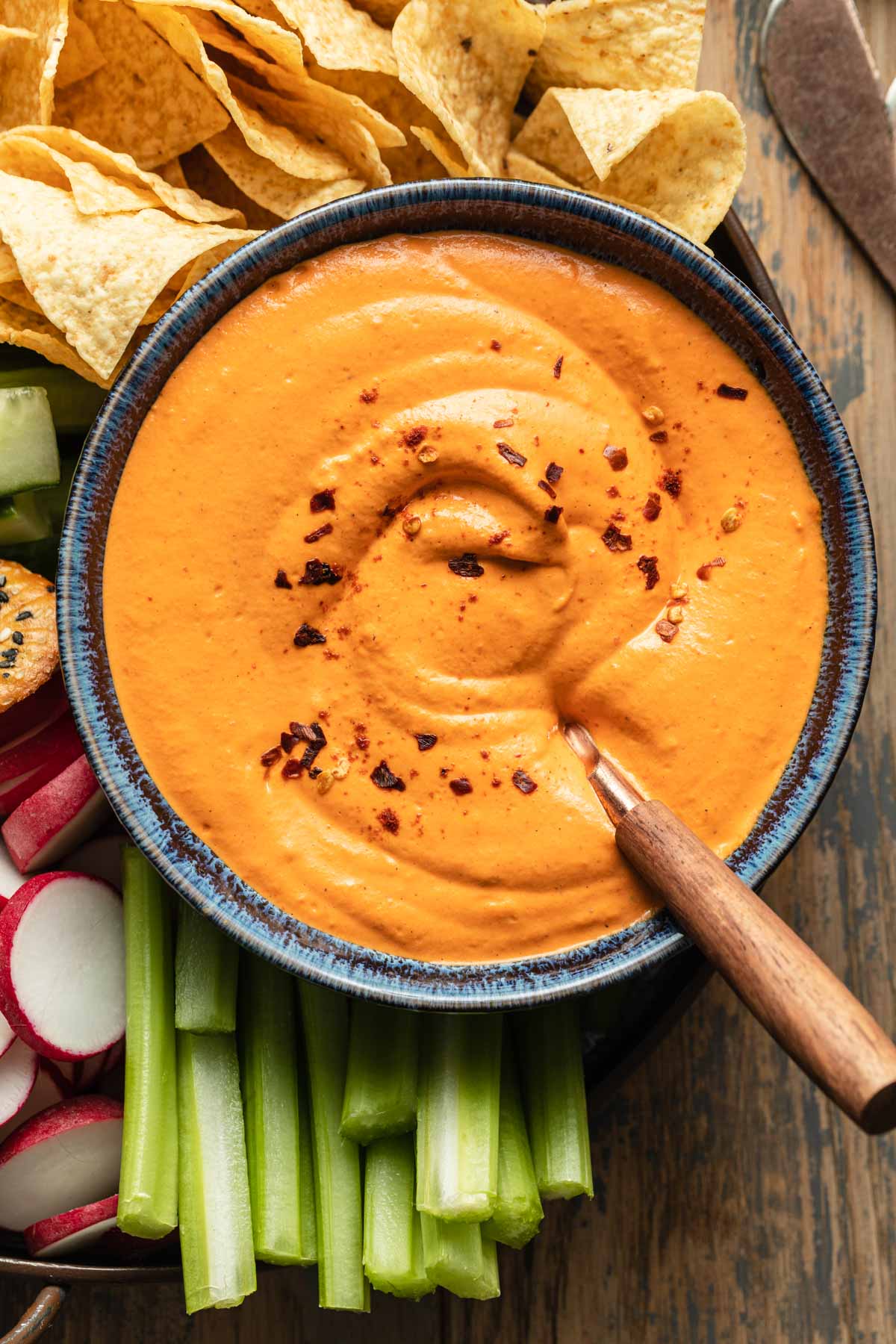 Close up view of red pepper dip in a blue bowl with a knife inserted into it.