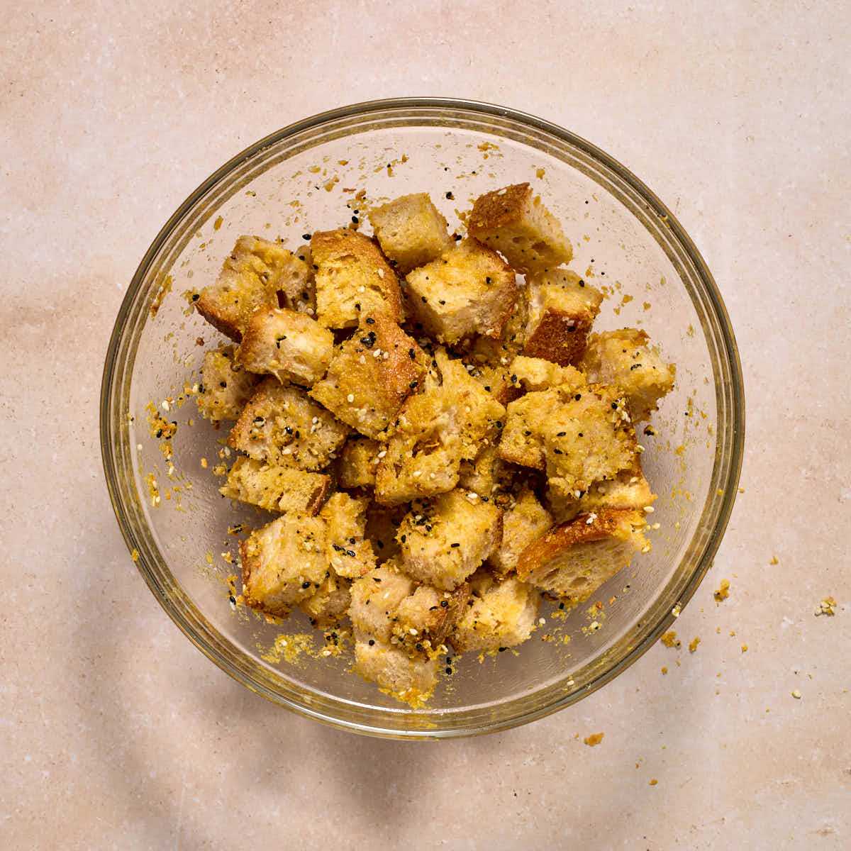 Bread cubes tossed with seasonings in a glass bowl.