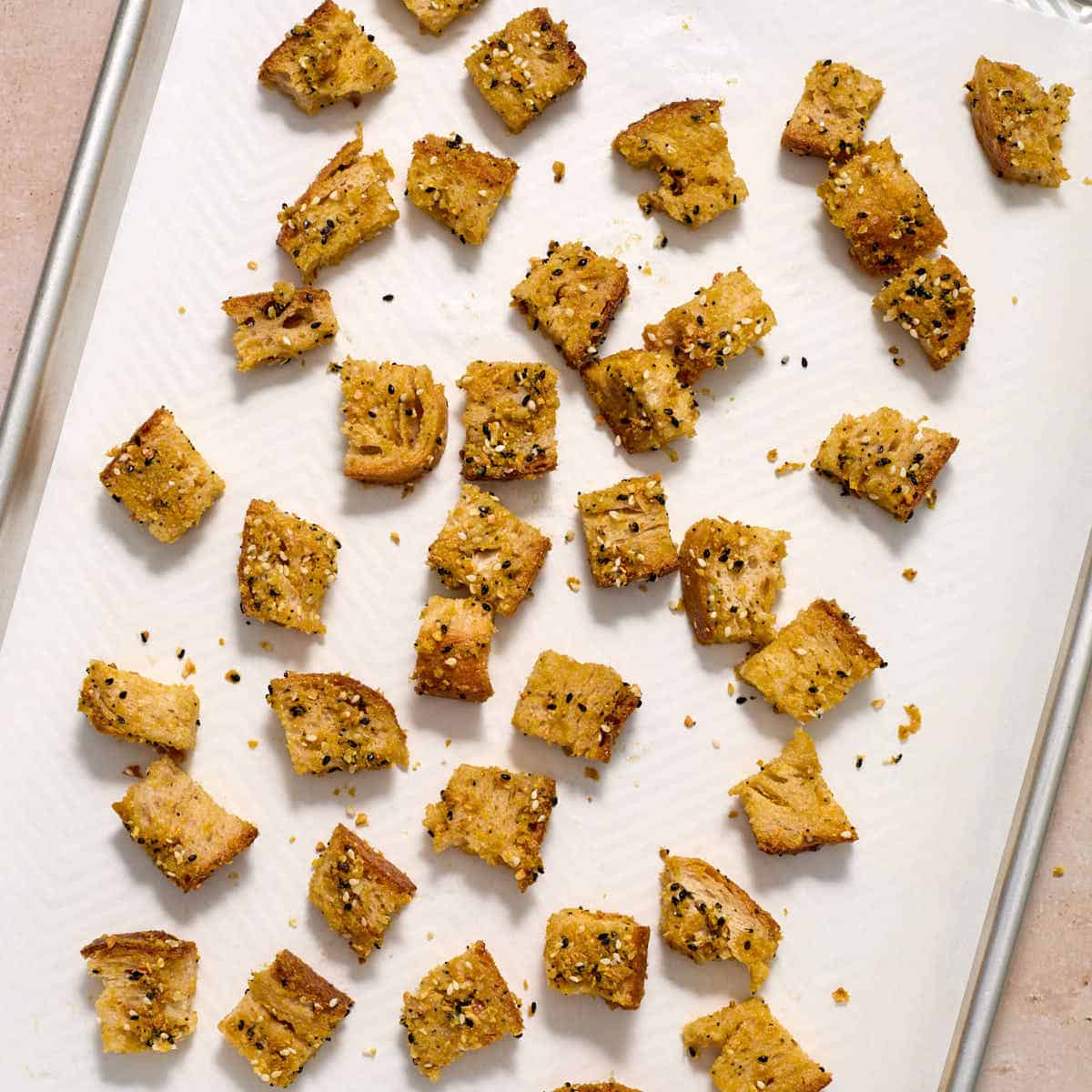 Seasoned bread cubes spread out on a parchment lined baking sheet.