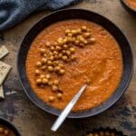 Overhead of tomato chickpea soup in a black bowl with a spoon and crispy chickpeas on top.