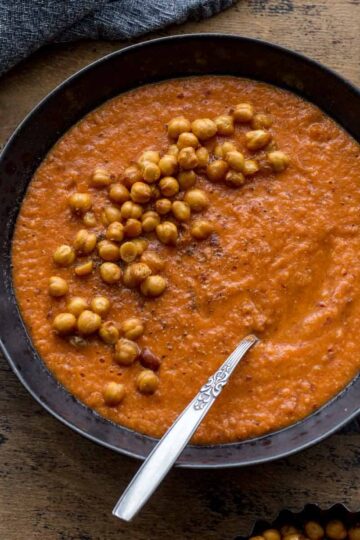 Overhead of tomato chickpea soup in a black bowl with a spoon and crispy chickpeas on top.