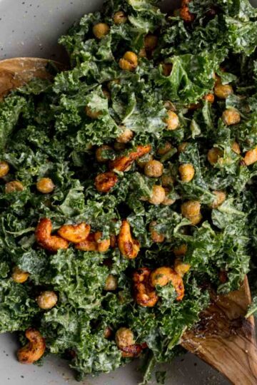 Close up of vegan kale caesar salad in a bowl with wooden serving spoons.