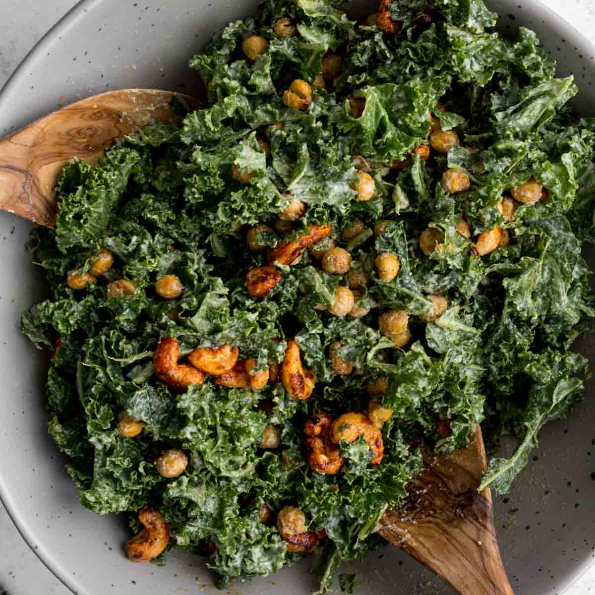 Close up of vegan kale caesar salad in a bowl with wooden serving spoons.