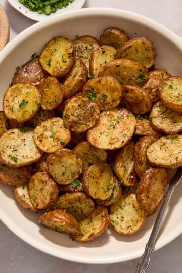 Air fryer baby potatoes served in a white bowl and topped with sea salt and chopped fresh parsley.