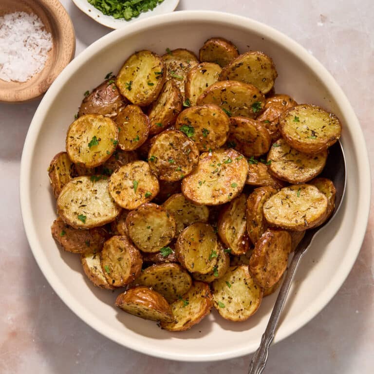Air fryer baby potatoes served in a white bowl and topped with sea salt and chopped fresh parsley.