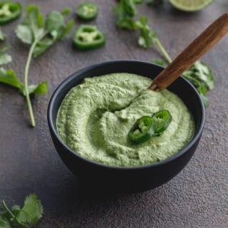 Creamy Jalapeño Dip in a small bowl on a grey surface with a serving spoon inserted into the bowl.