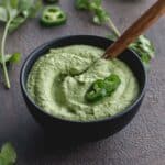 Angled view of creamy jalapeno dip in a small black bowl with jalapeno slices on top.