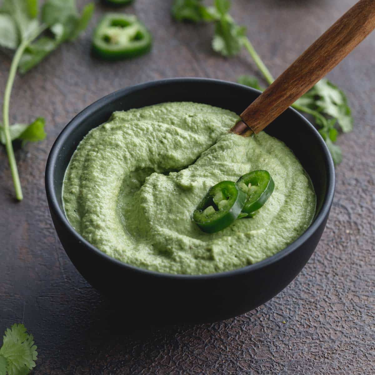 Angled view of creamy jalapeno dip in a small black bowl with jalapeno slices on top.