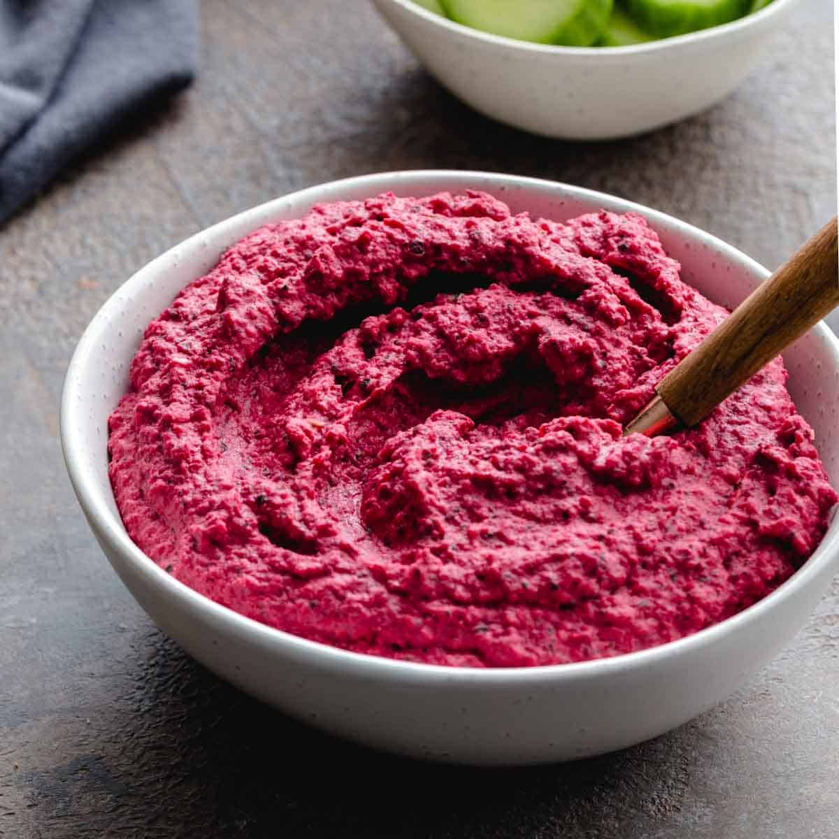 Side view of pink beet hummus in a white bowl.