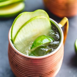 Green Apple Irish Mule in a copper mug and garnished with apple slices and lime wedges.
