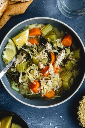 Overhead of lemon chicken orzo soup in a blue bowl with a spoon inserted into it.