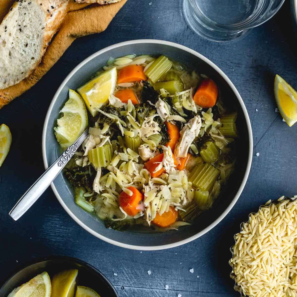 Overhead of lemon chicken orzo soup in a blue bowl with a spoon inserted into it.