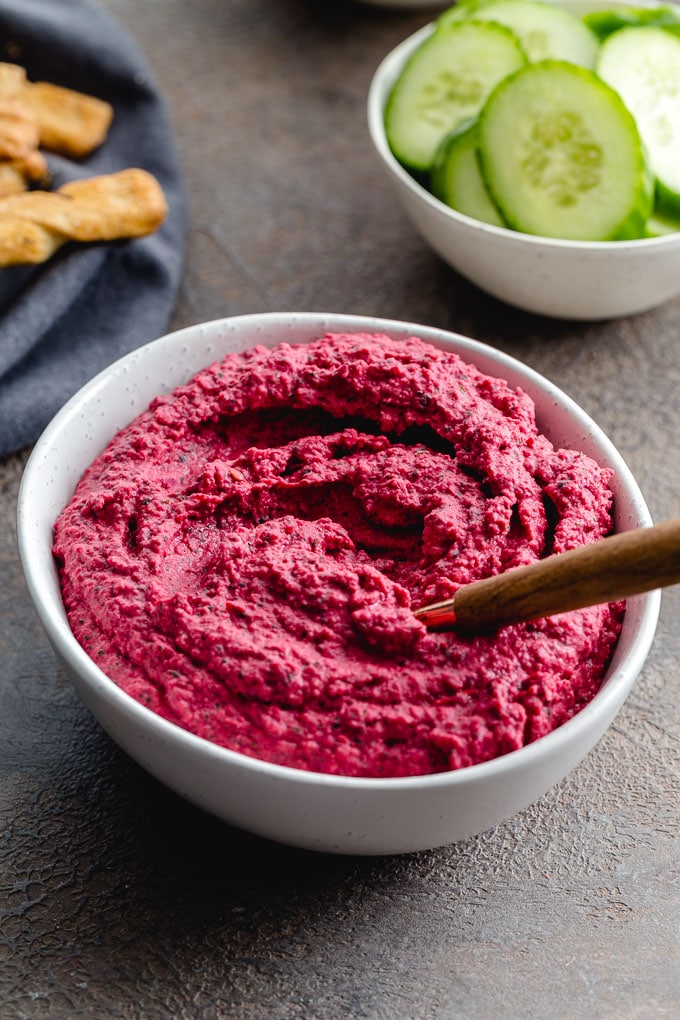 Up-close view of beet and white bean hummus swirled around in a white bowl with a serving knife.