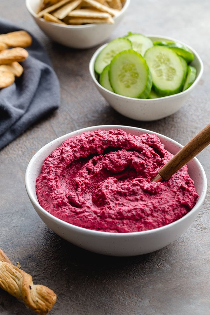 Up-close view of roasted beet hummus in a white bowl with cucumber slices in the background.