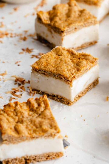 Angled view of carrot cake ice cream sandwiches cut into squares and arranged on parchment paper.
