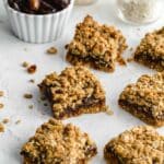 Healthy date squares arranged on parchment paper with dates and oats in the background.