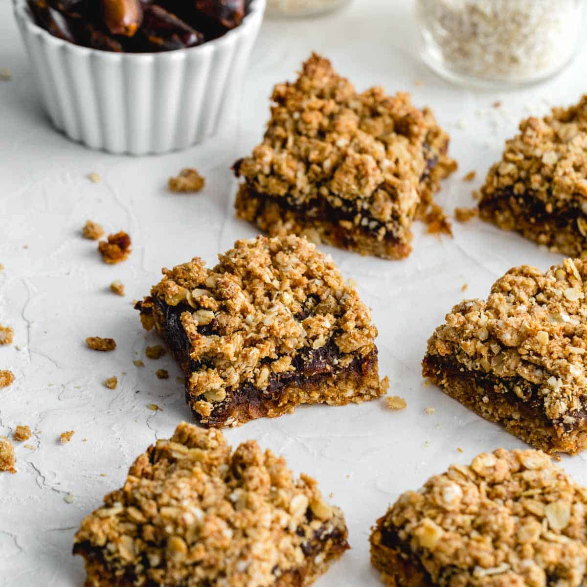 Healthy date squares arranged on parchment paper with dates and oats in the background.