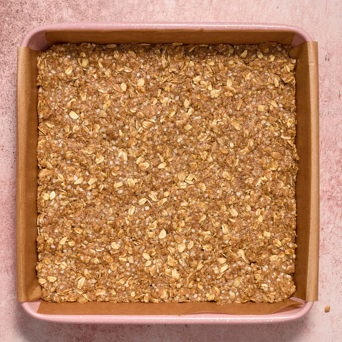 Some of the oat and quinoa mixture pressed into the bottom of a square pan.