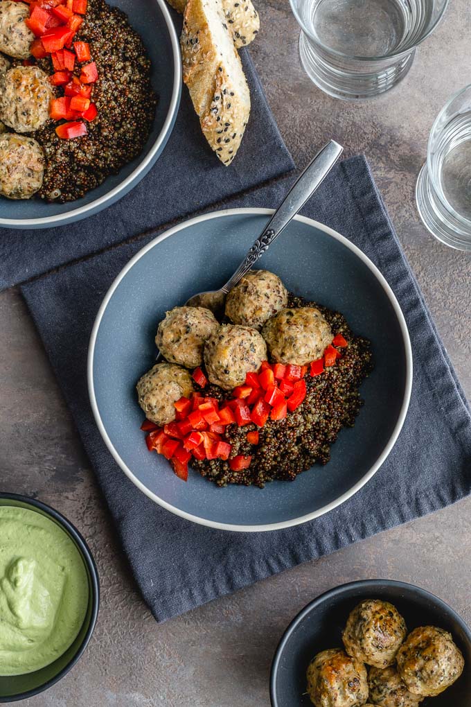 Healthy turkey meatballs served with quinoa and red peppers in blue bowls on grey napkins.