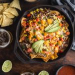 Loaded Veggie Nachos in a cast iron pan surrounded by dips, chips and beer.