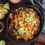 Overhead of loaded veggie nachos in a black cast iron skillet.