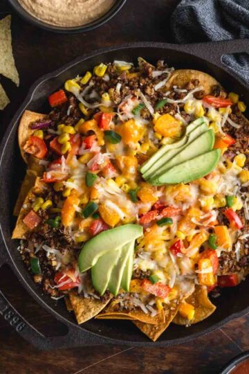 Overhead of loaded veggie nachos in a black cast iron skillet.