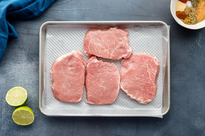 Raw pork chops arranged on a sheet pan.