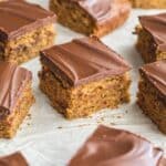 Angled view of square pieces of banana snack cake arranged on white parchment paper.