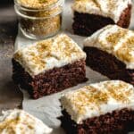Pieces of frosted chocolate sheet cake cut into squares and arranged on white parchment.