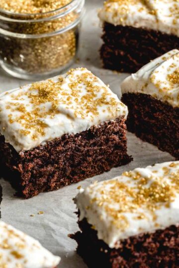 Pieces of frosted chocolate sheet cake cut into squares and arranged on white parchment.