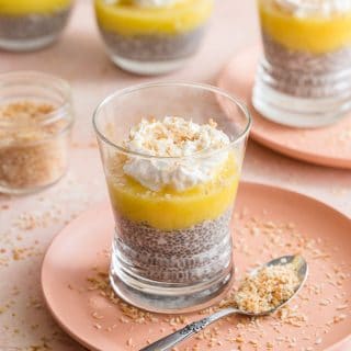 Pineapple Coconut Chia Pudding in a glass on a pink plate with other puddings in the background.