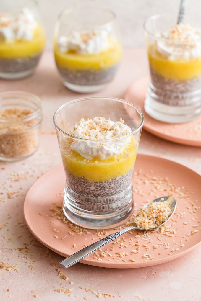 Glasses of coconut chia pudding with pineapple puree arranged on pink plates.