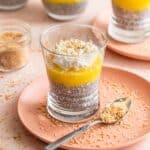 Side view of pineapple coconut chia pudding in a glass on a pink plate with toasted coconut around it.