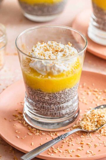 Side view of pineapple coconut chia pudding in a glass on a pink plate with toasted coconut around it.