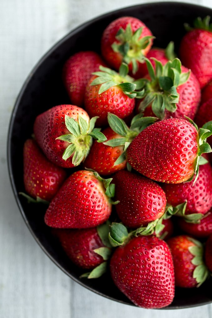 Up close overhead view of fresh strawberries in a black bowl.