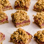 Strawberry oat bars arranged on parchment paper on a pink surface.