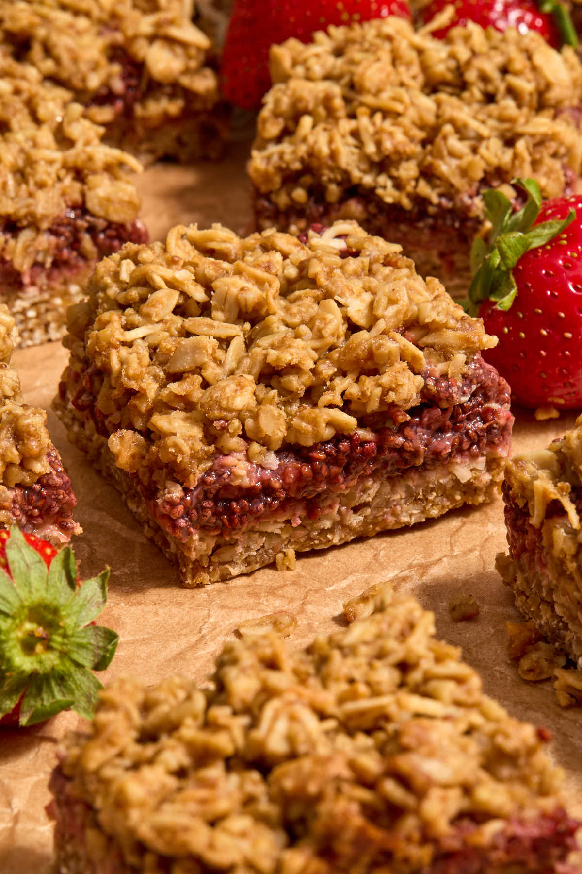 Oat bars on parchment paper with strawberries peaking in the frame.