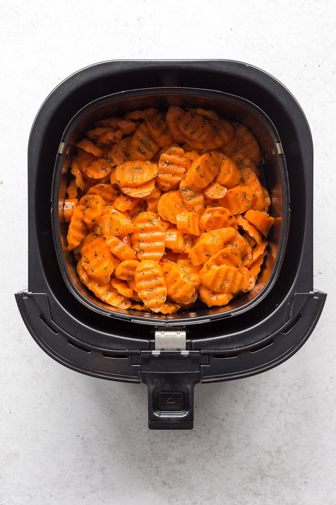 Overhead view of sliced raw carrots in the air fryer basket and covered in seasonings.