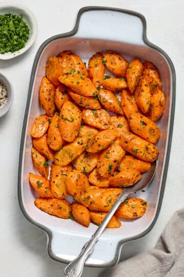 Air fryer carrots served in a white dish with fresh parsley and salt and pepper on the side.