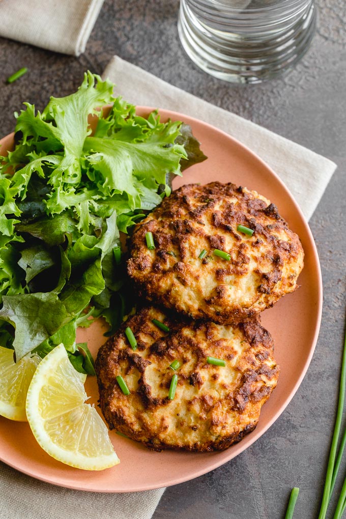 Up close photo of air fryer salmon cakes on a pink plate and topped with chives.