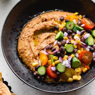 Up close view of a bowl of black bean hummus loaded with veggie toppings.
