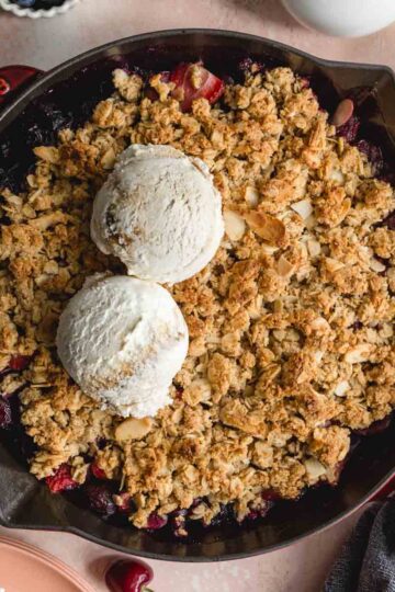 Overhead of almond cherry crisp in a skillet with 2 scoops of ice cream on top.