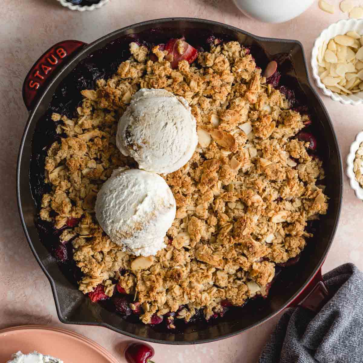 Overhead of almond cherry crisp in a skillet with 2 scoops of ice cream on top.