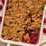 Gluten-free cherry crisp in a white baking dish with a serving spoon scooping some out.