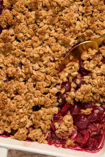 Gluten-free cherry crisp in a white baking dish with a serving spoon scooping some out.