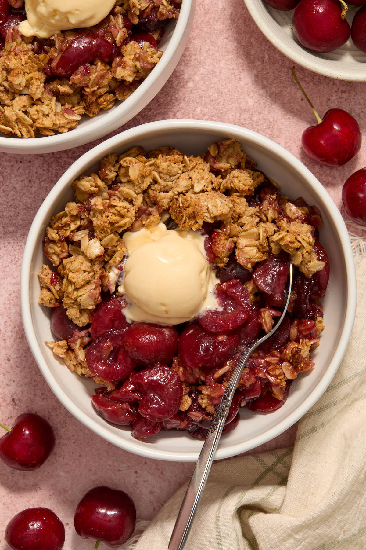 Cherry crisp served in a white bowl with a scoop of ice cream on top.