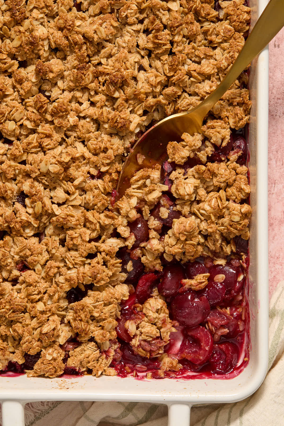 Cherry crisp in a white baking dish with a serving spoon inserted into it.